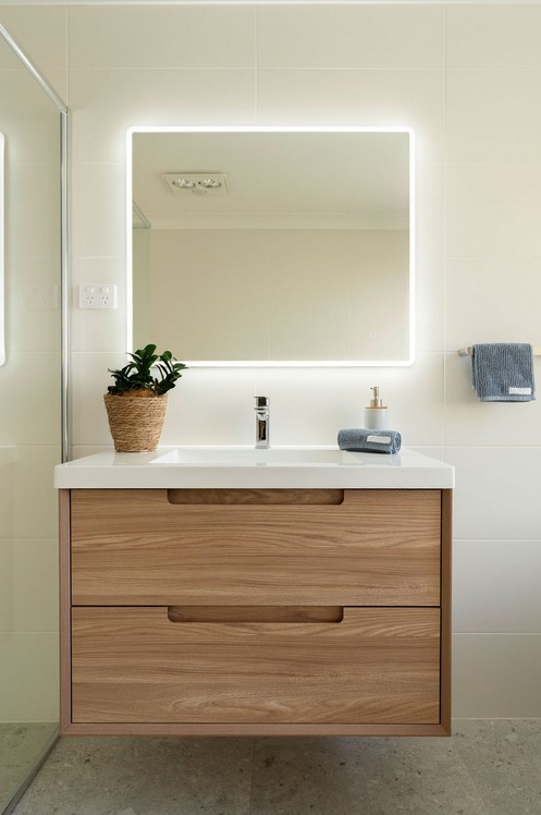 Floating timber vanity with a white top under a backlit square mirror